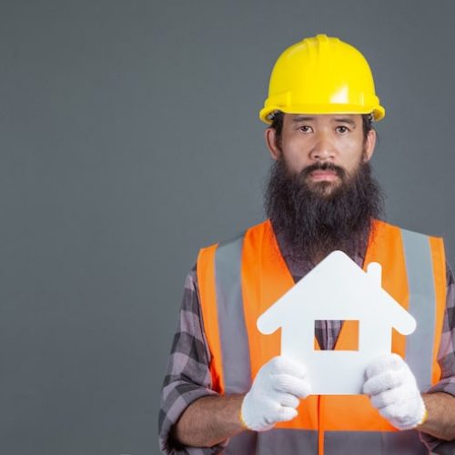 male-engineer-wearing-yellow-safety-helmet-holding-white-house-symbol-gray_1150-17345